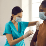 Black woman getting vaccine shot from a female health care professional wearing scrubs and gloves