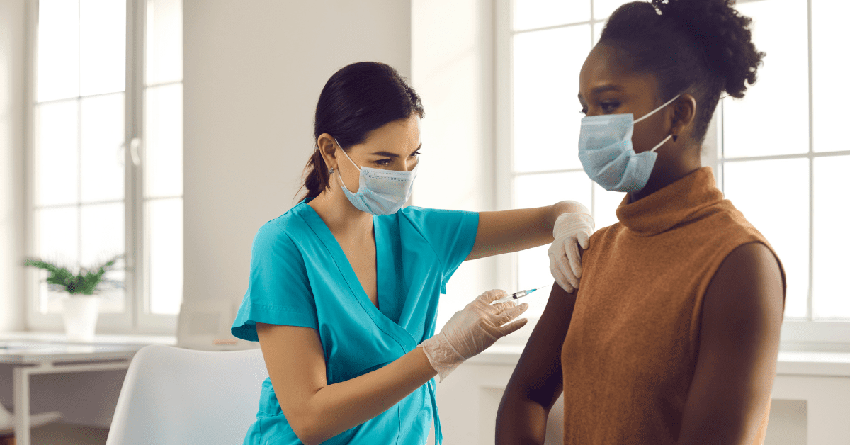 Black woman getting vaccine shot from a female health care professional wearing scrubs and gloves
