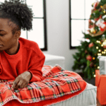Black woman in a red sweater sitting near Christmas tree pinching her nose