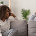 Black mother and daughter having a conversation on a gray couch
