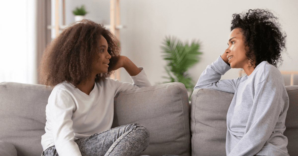 Black mother and daughter having a conversation on a gray couch