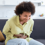 Black woman sitting on the couch, holding her stomach in pain