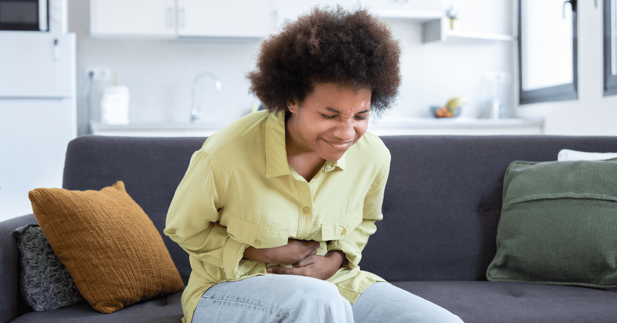 Black woman sitting on the couch, holding her stomach in pain