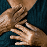 The image depicts a close-up of a woman's hands clasped against her chest.