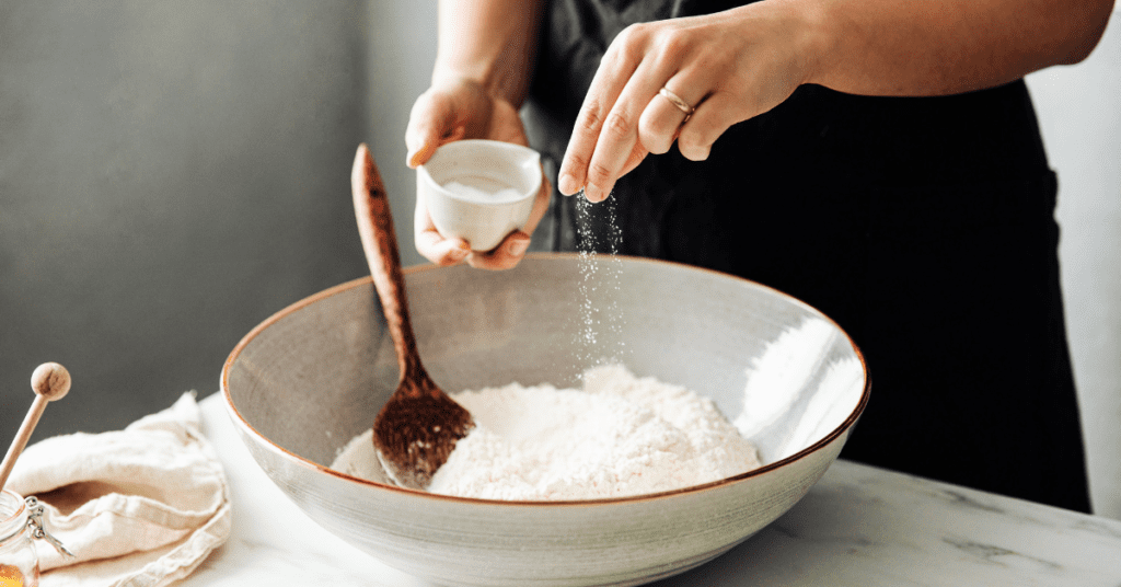 Closeup of woman’s hands sprinkling salt (sodium) over a bowl of flour