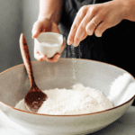 Closeup of woman’s hands sprinkling salt (sodium) over a bowl of flour