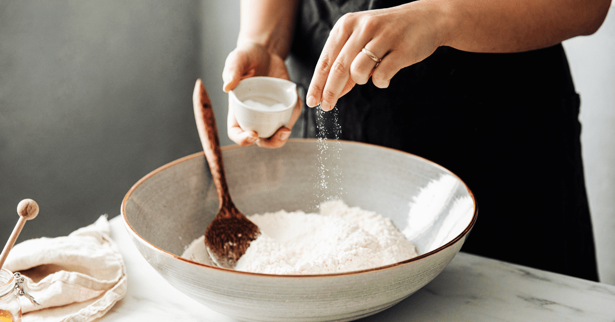 Closeup of woman’s hands sprinkling salt (sodium) over a bowl of flour