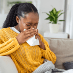 Black woman sitting on couch blowing her nose
