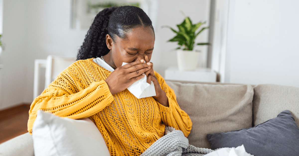 Black woman sitting on couch blowing her nose