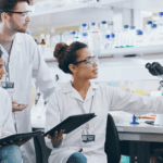 Group of scientists in lab coats gathered in front of a laptop