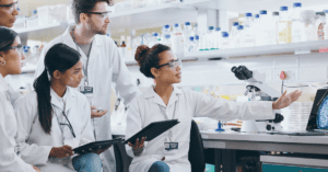 Group of scientists in lab coats gathered in front of a laptop