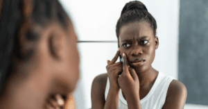 Young Black woman picking at skin in the mirror