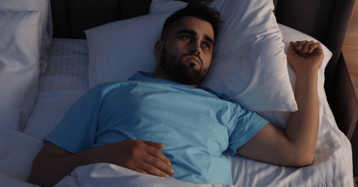 Man with beard laying in bed with a troubled look on his face.