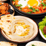 Plates of mediterranean food, including hummus and pita, falafel, and shakshuka