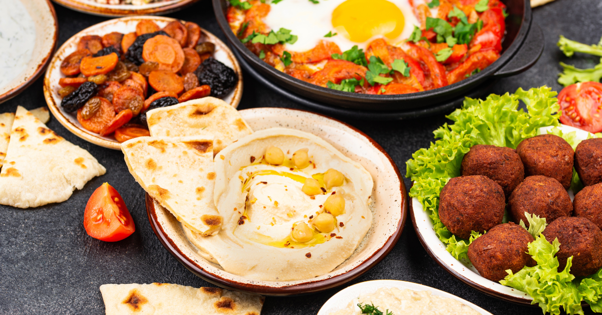 Plates of mediterranean food, including hummus and pita, falafel, and shakshuka