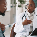 Black female doctor explaining asthma symptoms to Black man holding his chest