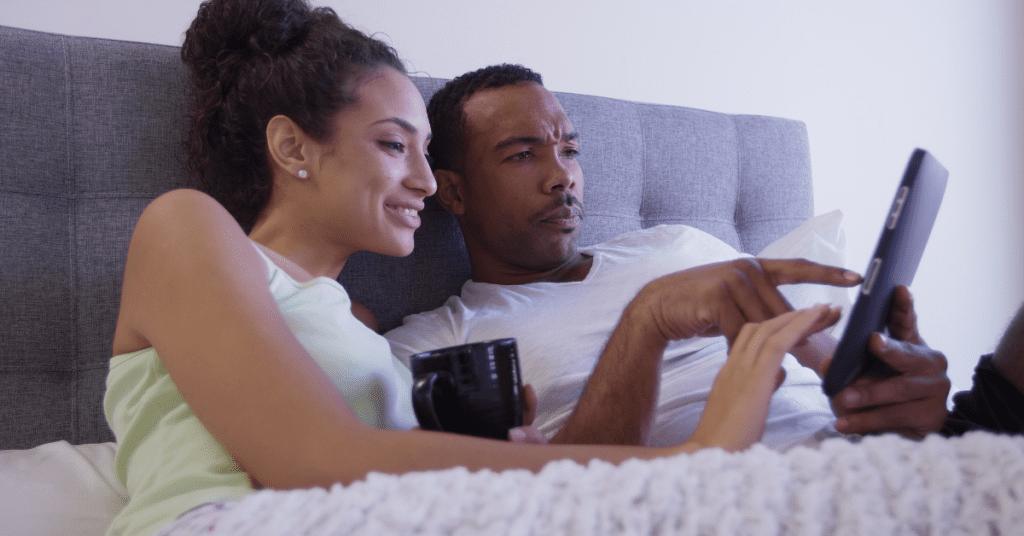 Man and woman sitting in bed, looking for information on their tablet device together