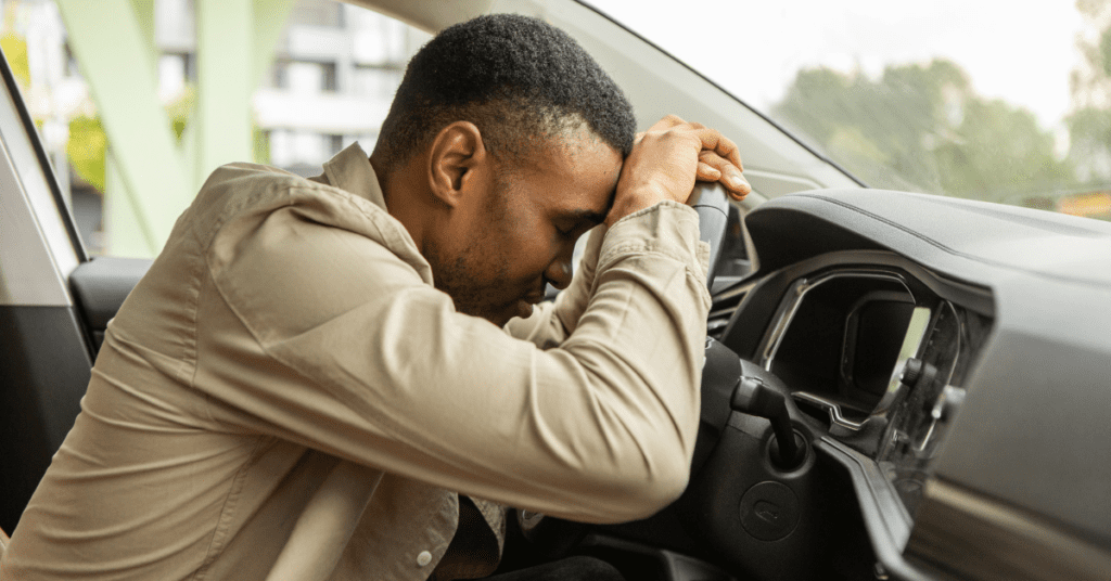 Black man in car, resting his head on the steering wheel
