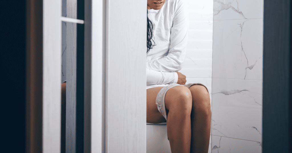 Half-body shot of woman sitting on the toilet holding her stomach