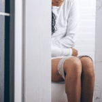 Half-body shot of woman sitting on the toilet holding her stomach