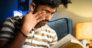 Young boy reading book and pressing one eye with his fingers