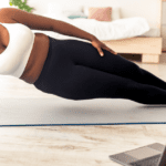 Woman following a fitness video on her laptop. She is in gym clothes doing a plank on a yoga mat.