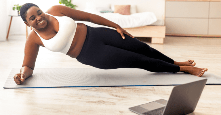 Post Holiday Detox Diet and How to Stick to It 1 Woman following a fitness video on her laptop. She is in gym clothes doing a plank on a yoga mat.