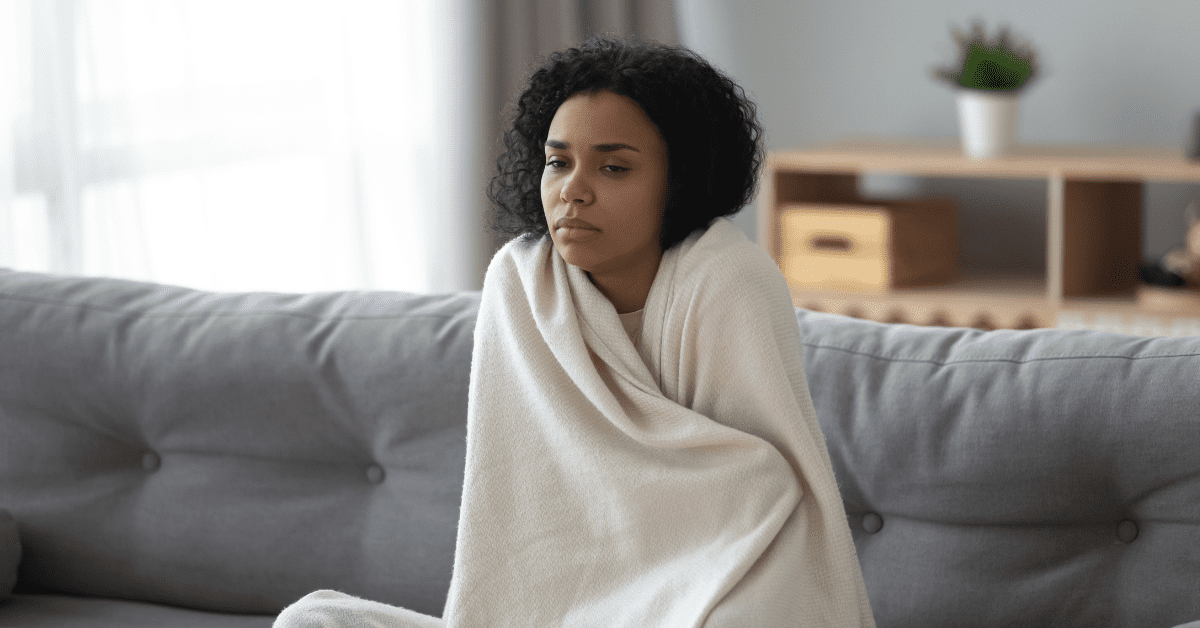 Woman wrapped in a blanket, sitting on the couch, and staring blankly into space