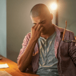 Young man with headache pinching his nose and holding his glasses
