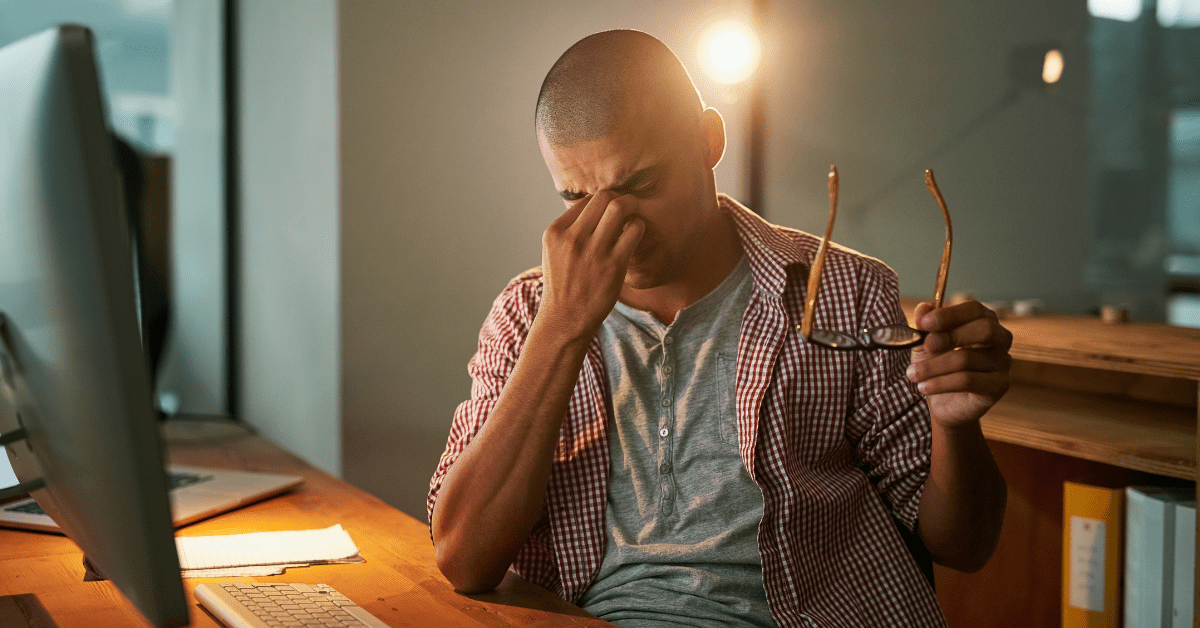 Young man with headache pinching his nose and holding his glasses