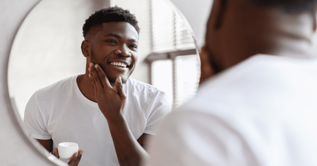 Black man looking in the mirror and applying a skincare product to his face