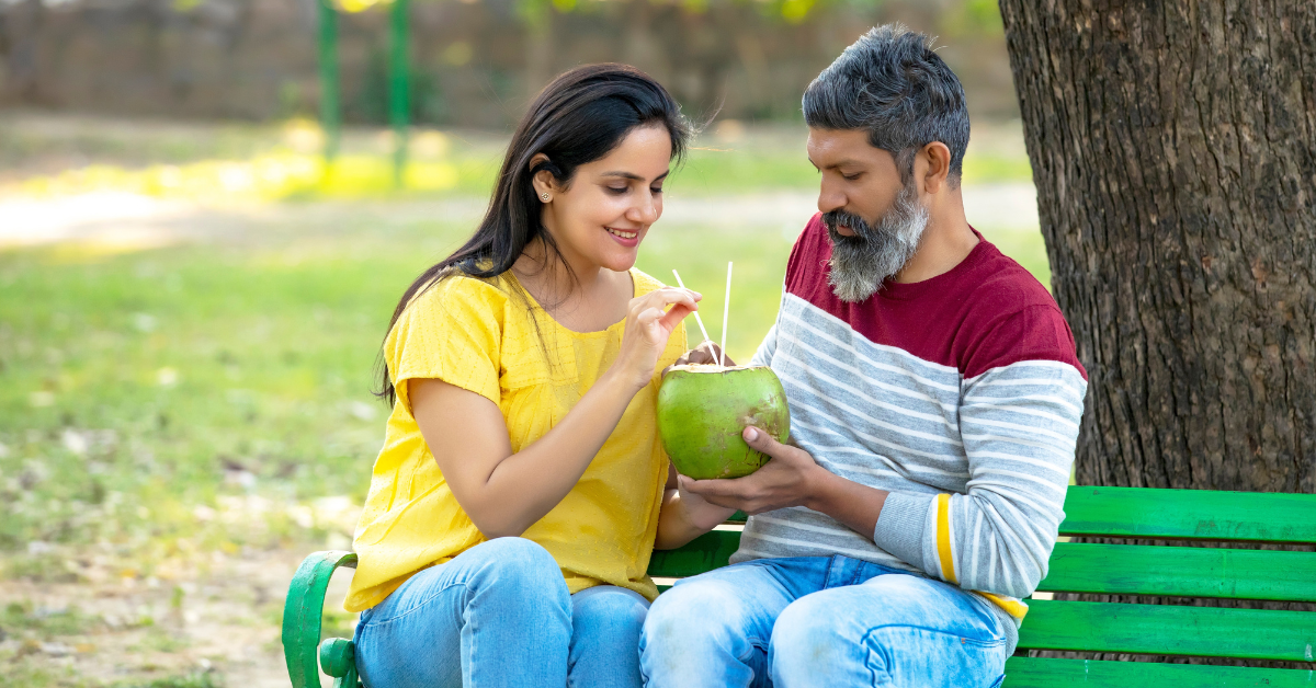 South asian couple sitting on a bench enjoying coconut water
