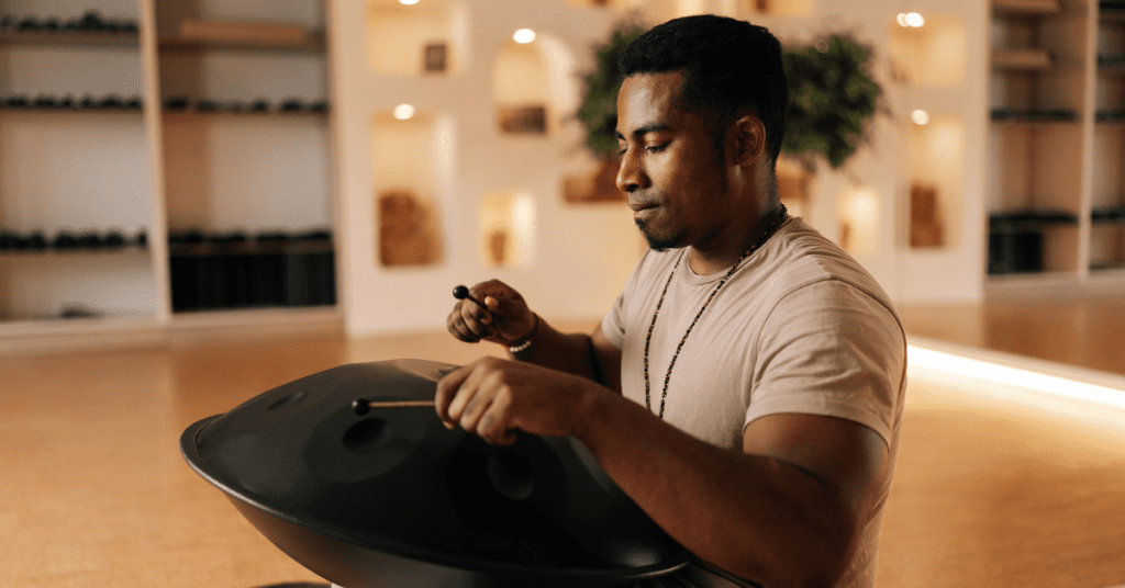 Black man meditating by using drumsticks on a metal drum circle