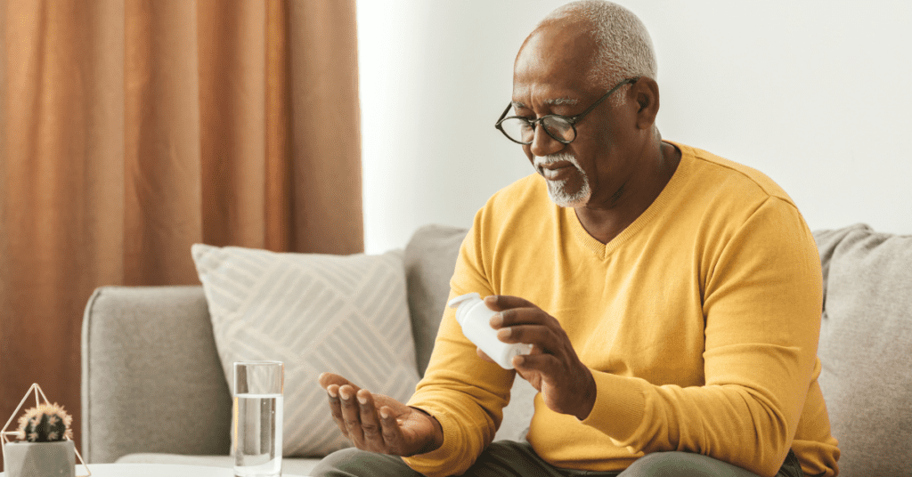 Elderly Black man with glasses holding a medicine bottle