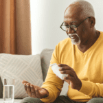 Elderly Black man with glasses holding a medicine bottle