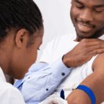 Close-up Of female doctor injecting Black male patient with syringe to collect a blood sample