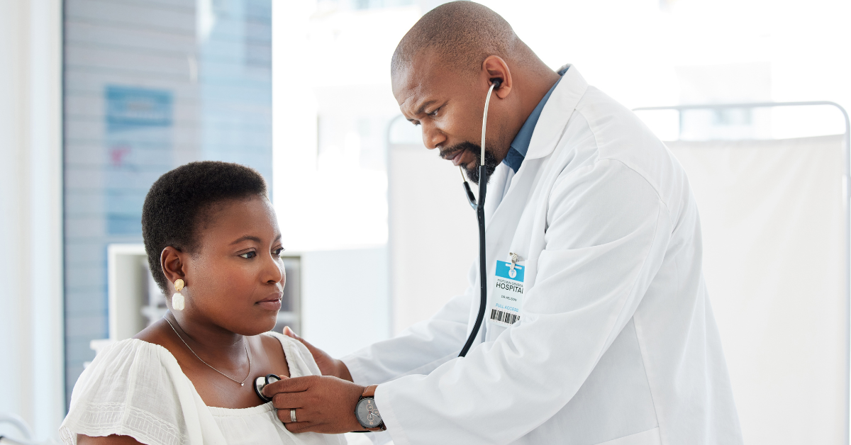 Doctor in a lab coat listening to patient’s heart using a stethoscope