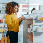 Black woman in a yellow sweater looking at a box of medications at the pharmacy