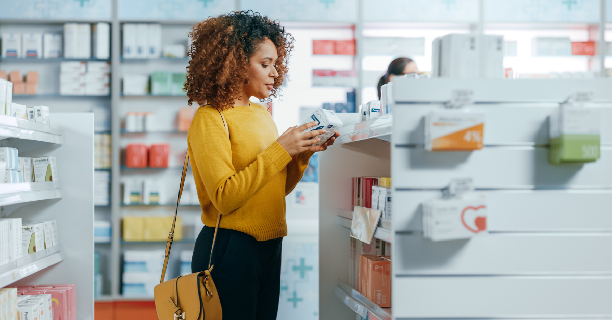 Black woman in a yellow sweater looking at a box of medications at the pharmacy