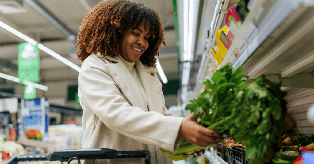 Smiling Black woman buying greens from the refrigerated section in the supermarket.