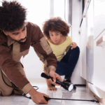 Young Black couple using a flashlight to check underneath their kitchen cabinets
