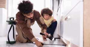 Young Black couple using a flashlight to check underneath their kitchen cabinets