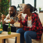 Young Black couple on the couch eating Chinese takeout with chopsticks
