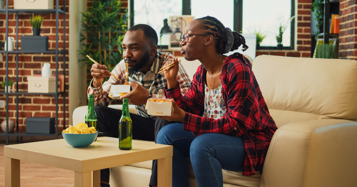 Young Black couple on the couch eating Chinese takeout with chopsticks