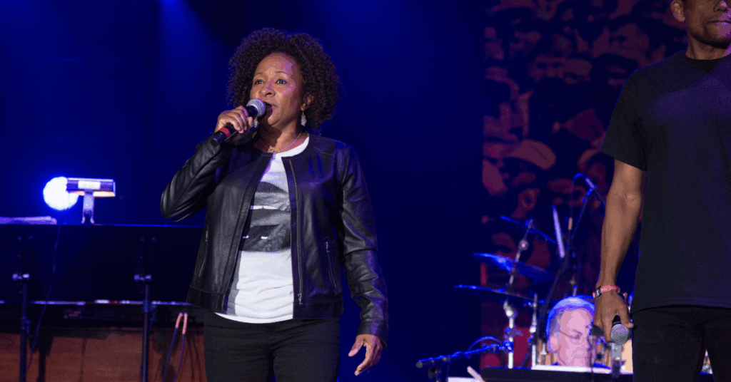 Comedian, Wanda Sykes, standing on a stage with a leather jacket and a mic in her hand