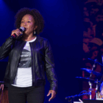 Comedian, Wanda Sykes, standing on a stage with a leather jacket and a mic in her hand