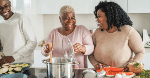 Black family of three cooking a heart failure friendly meal. The mom is stirring the pot while her daughter and son cut vegetables, like carrots and zucchinis, on either side of her.