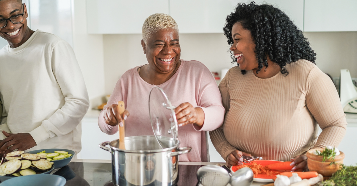 Black family of three cooking a heart failure friendly meal. The mom is stirring the pot while her daughter and son cut vegetables, like carrots and zucchinis, on either side of her.