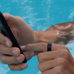 Close-up of a person’s hands in the swimming pool, wearing an oura ring and using their phone