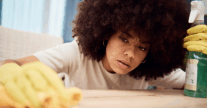 Close-up of young Black woman with an afro, wearing yellow gloves, and cleaning her shelf with a spray that contains forever chemicals (PFAS)